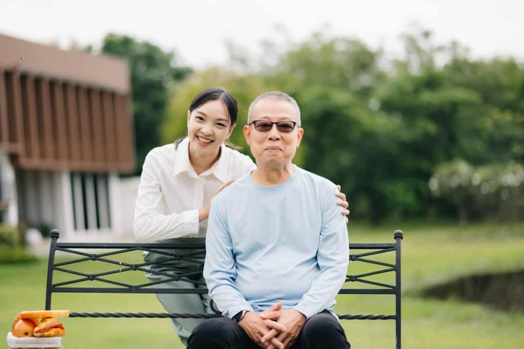Happy adult granddaughter and senior grandfather having fun enjoying talk while relaxing sitting outdoor at the park