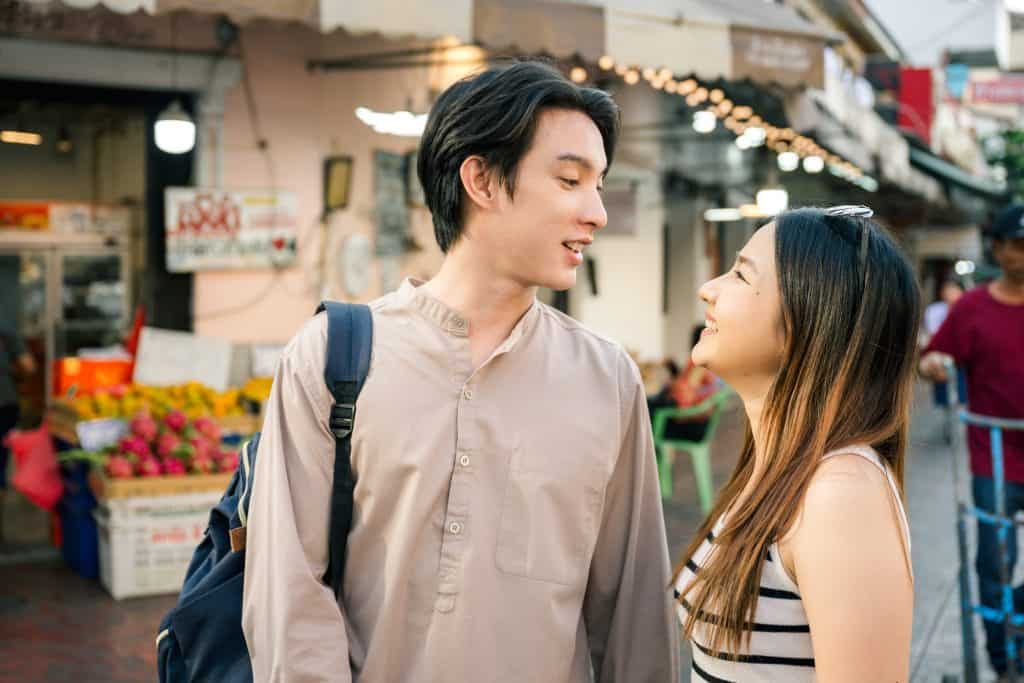 Happy asiancouple visiting a traditional market in bangkok, thailand, enjoying their summer holidays together and looking at each other. background typical bangkok street. 